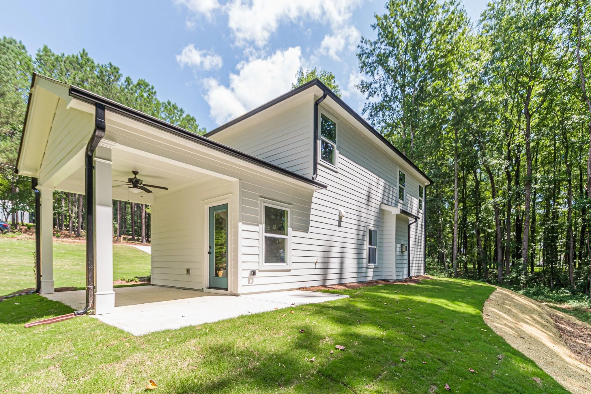 Side of the white house with a covered porch, ceiling fan, and glass door opening onto a concrete patio and lawn