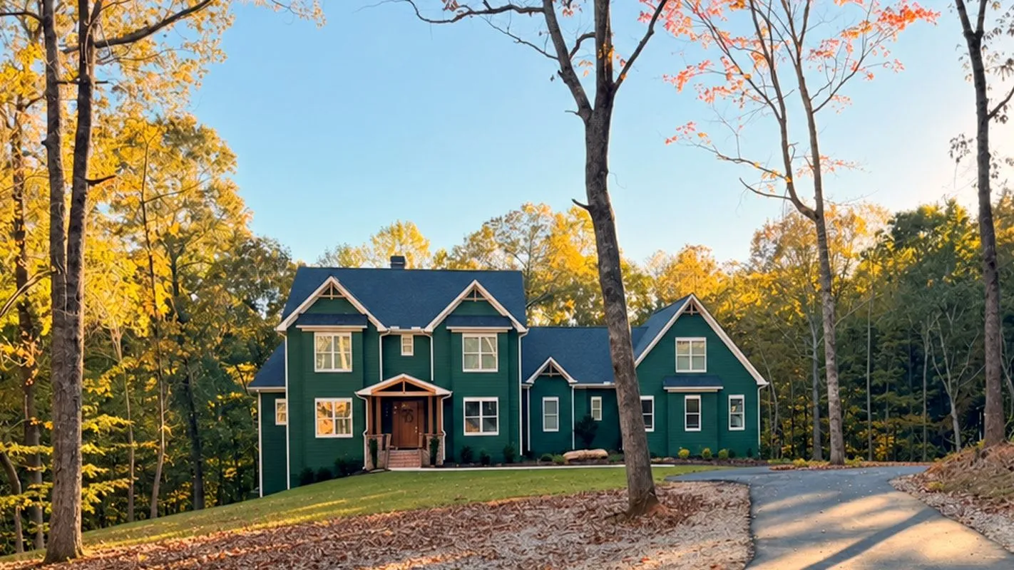 Dark green two-story house with white trim among tall trees in fall color, at the end of a curving driveway. Built by Daven Residential.